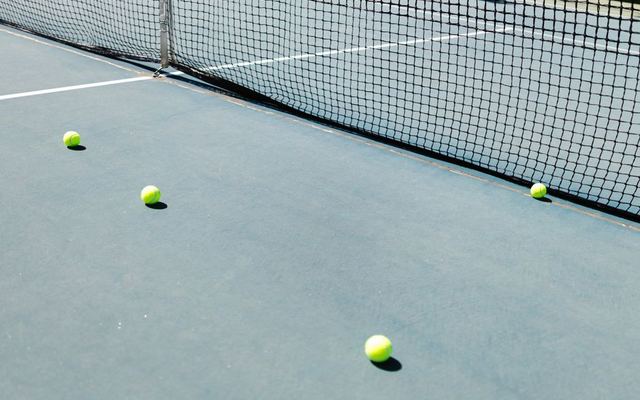 A tennis court featuring a net and several tennis balls lying on the ground, well-lit by sunlight.
