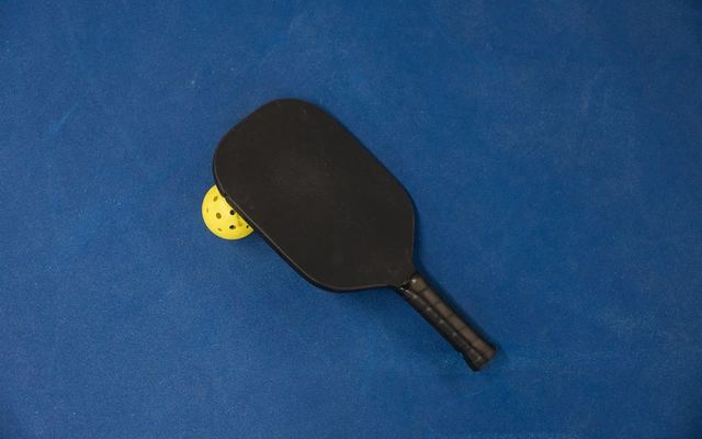 A pickleball paddle and ball on a textured blue surface, showcasing sports equipment.
