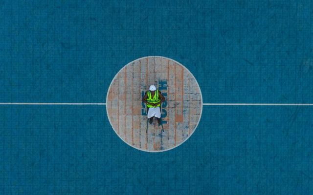Aerial shot of a worker in safety gear standing at the center of a basketball court.