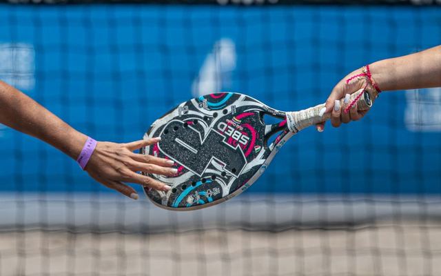 Close-up of two players exchanging a padel racket on an outdoor court.