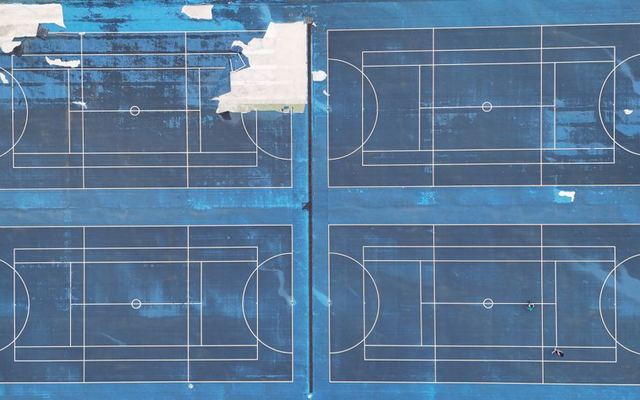 Drone shot of blue multi-sport courts with visible lines and wear from above.