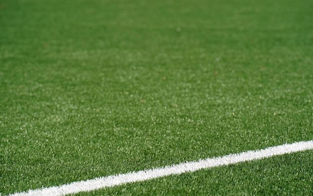 Close-up view of a green artificial soccer field with a white boundary line and space for text.