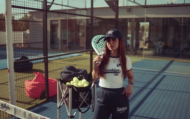 Young woman holding a padel racket, posing on a sunny sports court in Baghdad, Iraq.