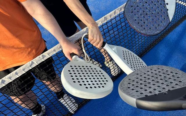 Padel players tapping rackets over a net on a blue court, symbolizing sportsmanship.