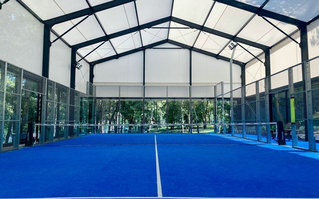 Spacious indoor padel court with vibrant blue flooring under a wide roof.