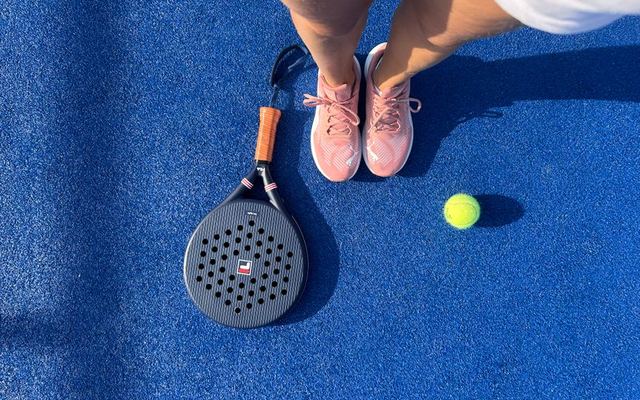 Top view of a padel player with shoes, racket, and ball on a vibrant blue court.