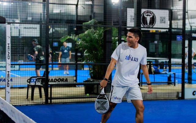 Energetic padel tennis player at indoor court mid-match.
