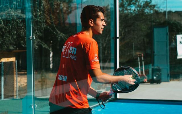 A focused young man practices padel tennis outdoors on a sunny day, showcasing skill and concentration.