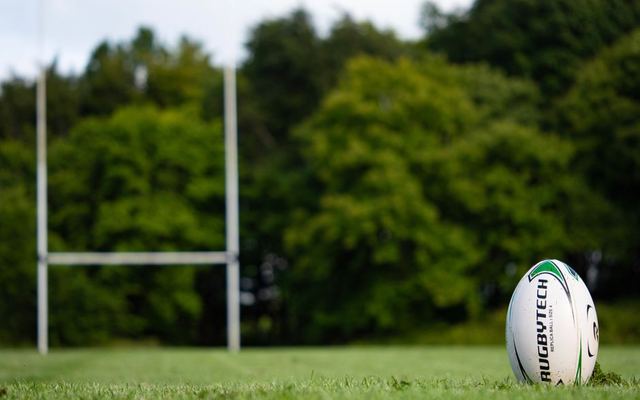 Rugby ball resting on a field in Galway, Ireland with goalposts in the background.