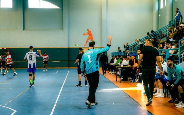 Dynamic handball match with players, referees, and spectators in a gymnasium.